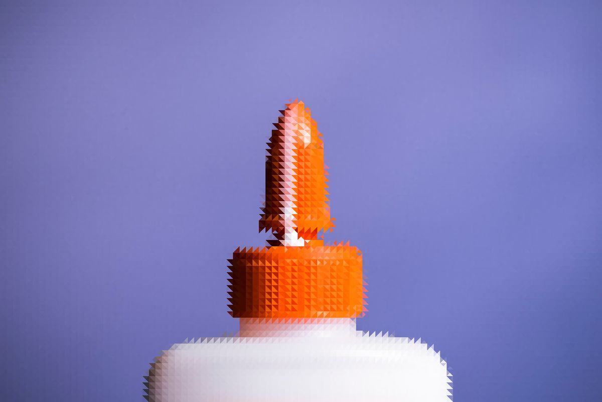 Picture of the top of a glue bottle. Orange tip. White body. Tip is open. There is a bead of glue running down the tip.